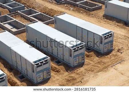 Containerized energy storage units installed in a construction site with sandy ground and concrete foundations