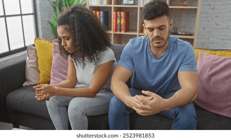 A contemplative couple sits apart on a gray sofa in a serene living room, conveying a sense of a troubled relationship. - Powered by Shutterstock