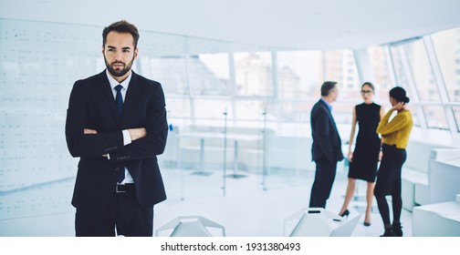 Contemplative male entrepreneur with crossed hands thoughtful looking away and thinking about business collaboration with blurred colleagues on background, Caucasian employer pondering in office