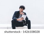 Contemplative man with digital tablet making virtual communication at social website while listening music audio songs via electronics headphones, Latino male in earphones pondering on publication