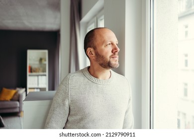 Contemplative man looking through window at home