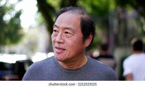 A Contemplative Middle Aged Asian Man Walking Outside In Sunlight Being Mindful. Portrait Of A Thoughtful Senior Person In City Street