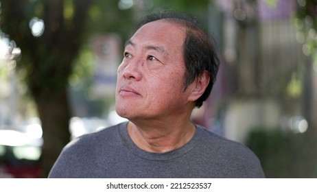 A Contemplative Middle Aged Asian Man Walking Outside In Sunlight Being Mindful. Portrait Of A Thoughtful Senior Person In City Street