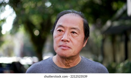 A Contemplative Middle Aged Asian Man Walking Outside In Sunlight Being Mindful. Portrait Of A Thoughtful Senior Person In City Street