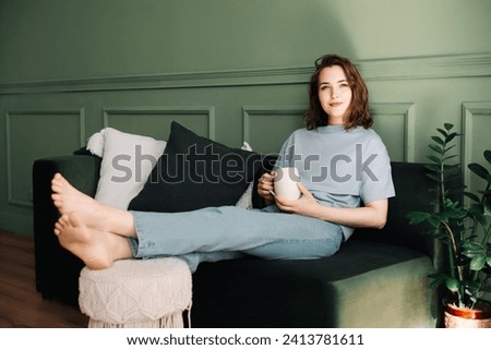 Contemplative Middle-Aged Woman Relaxing with Tea on Couch, Pensive, Gazing into Open Space. Reflective Moment: Thoughtful Woman Resting and Pondering on Sofa with Cup of Tea