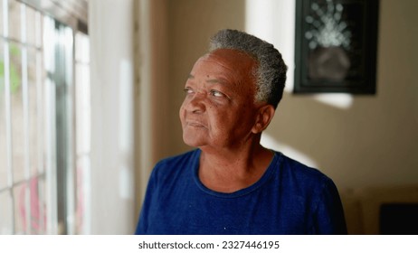 Contemplative Senior woman stands by window staring outside at home. Thoughtful pensive expression of an African American elderly person in 70s - Powered by Shutterstock