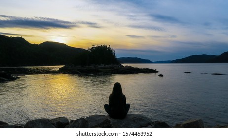 Contemplative woman sitting in a shore in front of the beautiful fjord of Saguenay at Petit-Saguenay - Shutterstock ID 1574463952