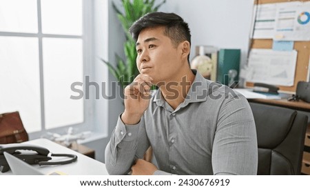 A contemplative young asian man in an office setting with a focus on business and professionalism, exuding a sense of thoughtfulness and career orientation.