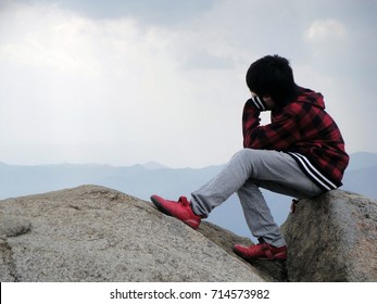 Contemplative young boy, lost in thought, sitting on rocks on top of a mountain staring into the distance