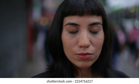 Contemplative young hispanic woman closing eyes in street. South American adult person with indigenous traits opening eye smiling. Portrait face closeup in urban environment - Shutterstock ID 2214716217