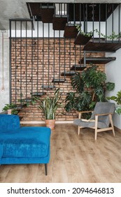 Contemporary armchair and sofa in cozy loft styled duplex flat with stairs and plants. Home environment. Luxury apartment for sale. Modern house with stairs interior design