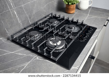 Contemporary black tempered glass gas stove hob with wok burner with auto ignition knob cast iron pan supports and flame safety valve built in compact high pressure laminate HPL countertop.