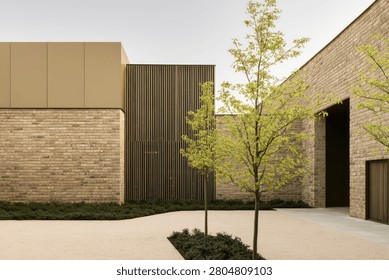 A contemporary building facade featuring brickwork, metal panels, and young trees, showcasing modern architectural aesthetics.