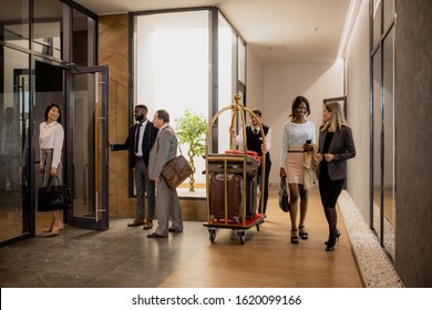 Contemporary business people communicating while porter moving among them and pushing cart with baggage inside hotel - Powered by Shutterstock