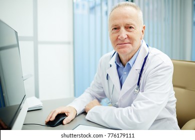 Contemporary Clinician In Uniform Sitting By Desk In Front Of Computer Monitor