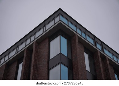 Contemporary corner building featuring sharp angular design with red brick facade, floor-to-ceiling glass windows, and black metal balconies in Wroclaw, Poland, under overcast sky