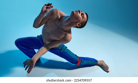 Contemporary dance style. Young shirtless man dancing, performing contemp, experimental dance over blue studio background. Concept of art, body aesthetics, motion, action, inspiration. - Shutterstock ID 2254709557