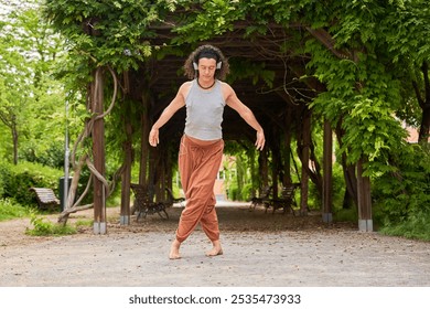 A contemporary dancer moves gracefully in a park, immersed in music through headphones, blending artistry with nature's serenity. - Powered by Shutterstock