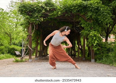 A contemporary dancer moves gracefully in a park, immersed in music through headphones, blending artistry with nature's serenity. - Powered by Shutterstock