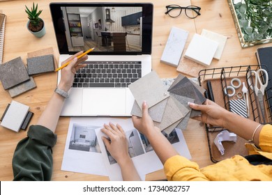 Contemporary Designer Pointing At Home Interior Example On Laptop Display While Consulting With Colleague Holding Linoleum Samples