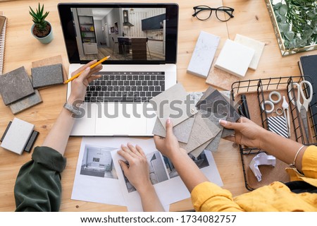 Contemporary designer pointing at home interior example on laptop display while consulting with colleague holding linoleum samples