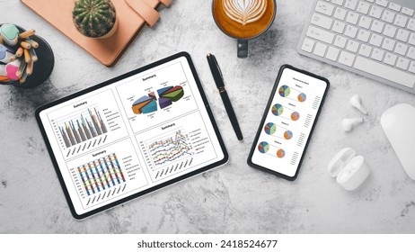 A contemporary desk setup featuring an array of devices displaying colorful statistical data, complemented by a cup of latte art coffee.