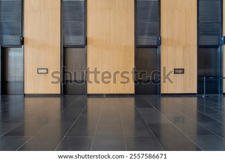 Contemporary elevator lobby featuring three modern elevators with polished metal doors. The lobby is adorned with elegant wooden paneling on the walls minimalistic and professional environments.