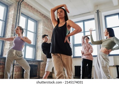 Contemporary female performer in activewear keeping right arm over her head while learning new movements of vogue dancing