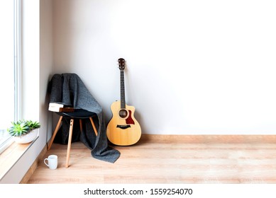 Contemporary home interior. Black chair covered with woolen gray blanket and acoustic guitar in front of an empty white wall. Time for hobby and leasure. - Powered by Shutterstock