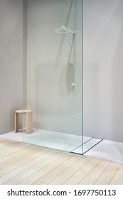 Contemporary Illuminated Interior With Light Walls, Glass Partition And A Wooden Floor. There Is A White Shower And A Wood Stool. Vertical.