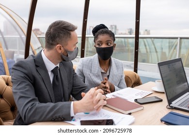 Contemporary Intercultural Business Partners In Formalwear And Protective Masks Discussing Financial Data At Meeting