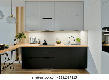Contemporary kitchen in black and grey colours with built in appliances, wooden dining table top and decorative slats