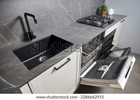 Contemporary kitchen with built-in opened dishwasher oven square black sink gas hob with grey porcelain stoneware countertop and cabinets.