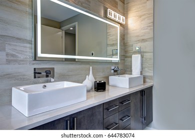 Contemporary master bathroom features a dark vanity cabinet fitted with rectangular his and hers sink and modern wall mount faucets under large mirror. Northwest, USA