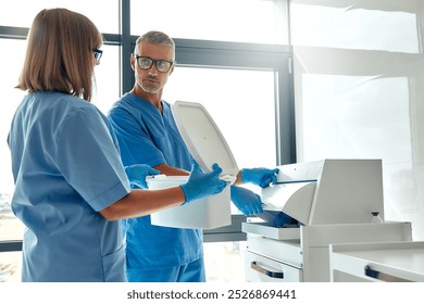 In a contemporary medical facility, two dedicated healthcare professionals, dressed in scrubs, engage in a detailed discussion while skillfully handling various lab equipment and instruments - Powered by Shutterstock