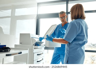 In a contemporary medical facility, two dedicated healthcare professionals, dressed in scrubs, engage in a detailed discussion while skillfully handling various lab equipment and instruments - Powered by Shutterstock