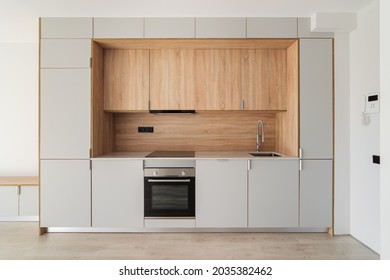 Contemporary Minimal Kitchen At Empty Refurbished Apartment. Wooden Furniture And Modern Appliances