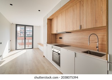 Contemporary Minimal Kitchen And Living Room With Balcony At Empty Refurbished Apartment. Wooden Furniture And Modern Appliances