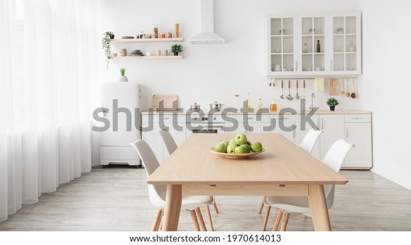 Contemporary minimalist interior of\
kitchen and dining room. White furniture with utensils and dinner\
table with chairs in Scandinavian style. Modern light\
design