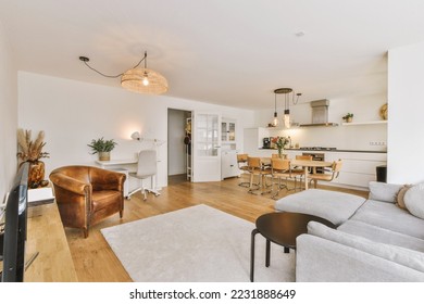 Contemporary minimalist style interior design of light studio apartment with wooden table and chairs in dining zone between open kitchen and living room with white walls and parquet floor