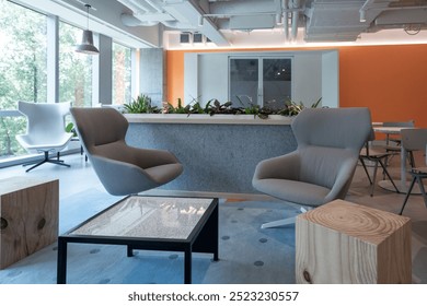 A contemporary office lounge area with comfortable, modern armchairs in muted tones, set around a glass-top coffee table. A backdrop of large windows floods the space with natural light, - Powered by Shutterstock