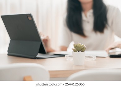 A contemporary office scene featuring a tablet and a small succulent plant on a wooden desk, with a blurred background. - Powered by Shutterstock