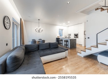 Contemporary open space living room and kitchen design featuring modern furniture, a stairway, and sleek decor in soft neutral colors for a stylish and inviting home environment. - Powered by Shutterstock