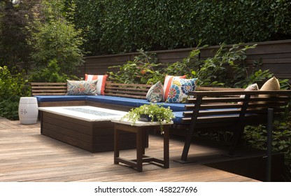 A contemporary outdoor conversation bench with pillows on a wooden deck.