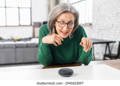 Contemporary Retired Woman Using Voice Commands To Control Smart Speaker, Mature Woman Talking To The Digital Virtual Assistant At Home, Asking A Question Or Requesting To Switch Music