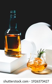 Contemporary Still Life With Whiskey, Scotch Or Bourbon Glass With Rosemary, Shard Ice On Black White Background With Geometric Cubes And Circles