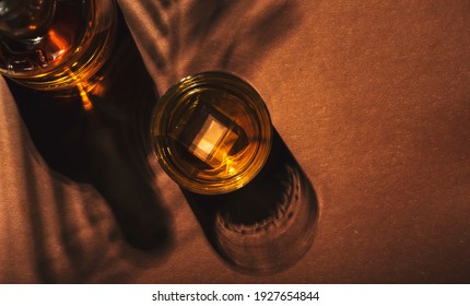 Contemporary still life with whiskey, scotch or bourbon glass with ice on textured brown background with hard lights and shadows, top view, copy space