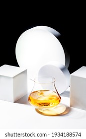 Contemporary Still Life With Whiskey, Scotch Or Bourbon In Glass With Shard Ice On Black White Background With Geometric Cubes And Circles