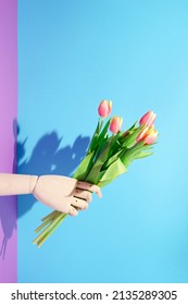 Contemporary still life, wooden mannequin hand holding  bouquet of orange - yellow tulips on blue - violet background. Minimal spring concept.