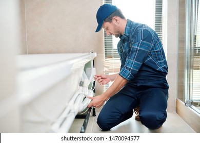 Contemporary technician in workwear installing pipe system by bathtub